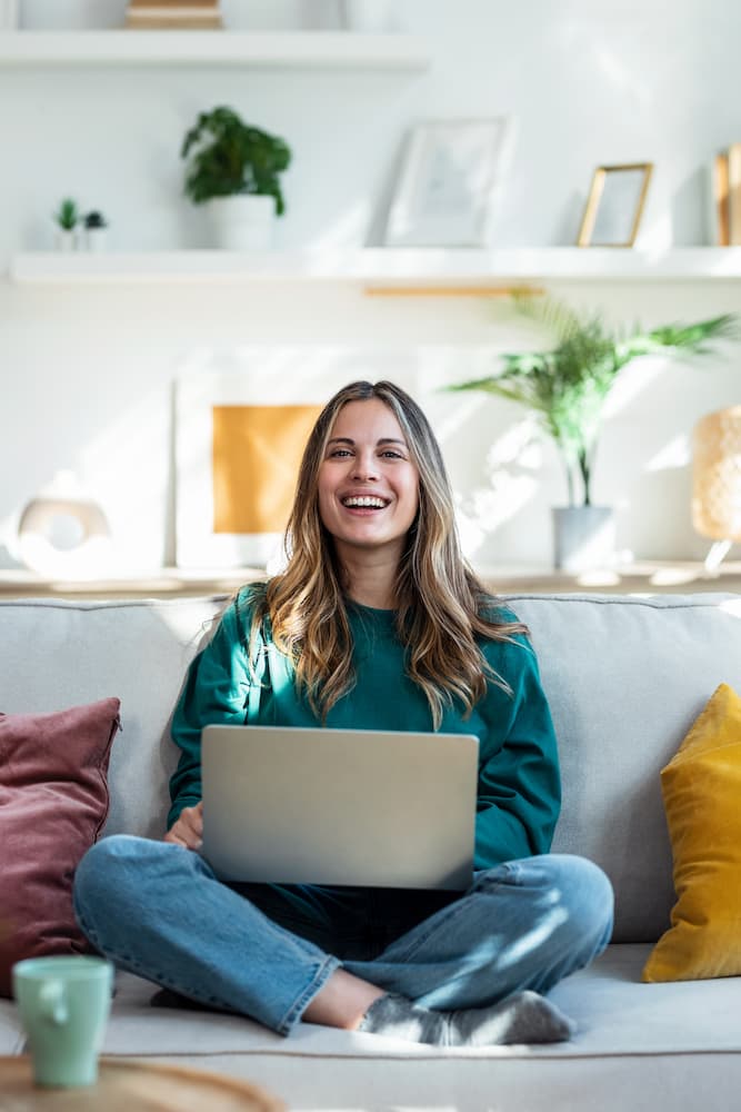 Frau sitzt auf Sofa und vergleicht Strompreise am Laptop